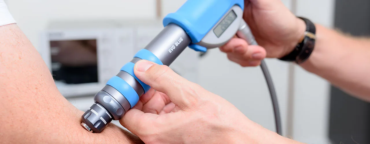Medizinisches Handgerät zur Stoßwellentherapie wird an einer Körperregion eingesetzt.